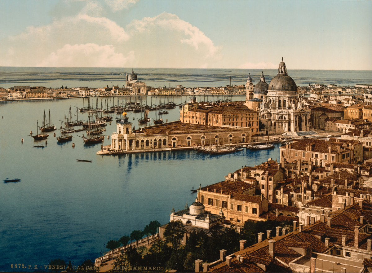 An elevated view takes in Venice’s domed waterfront churches, terracotta rooftops and sailing vessels across a pale blue lagoon.
