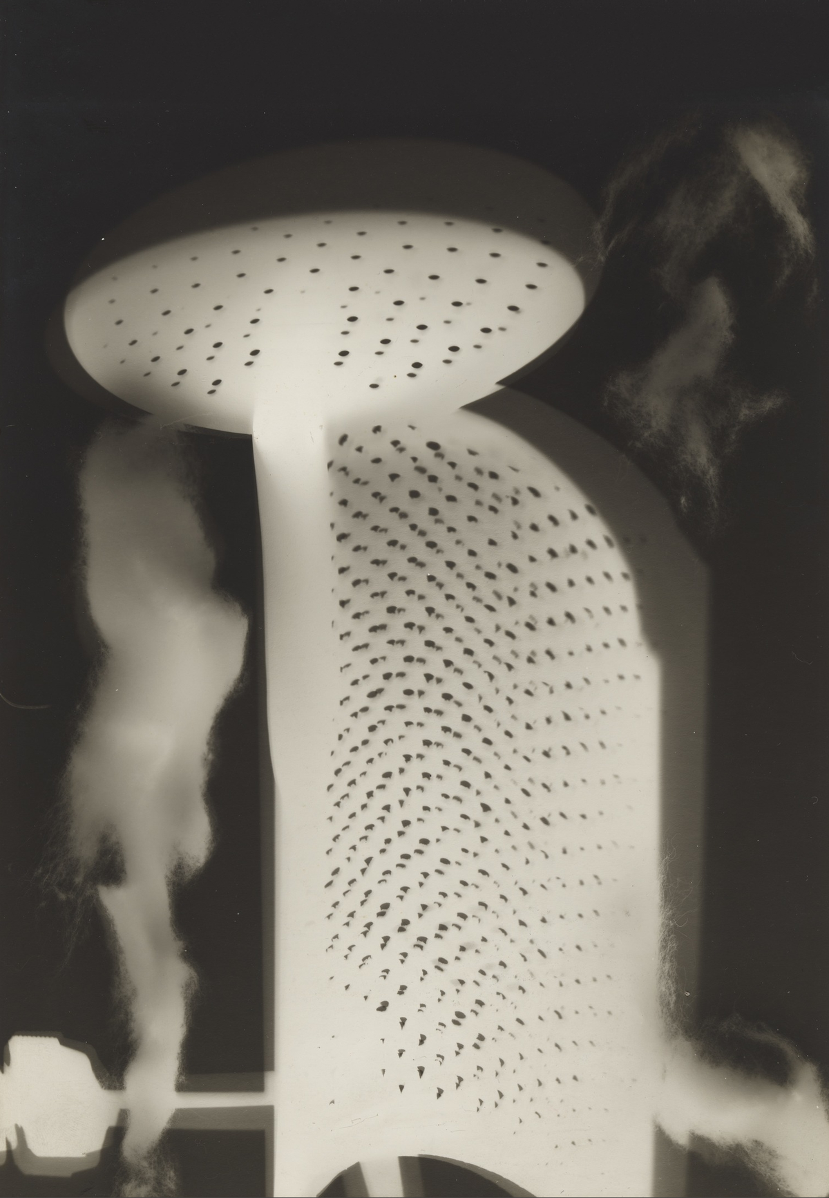 Pale perforated circular and curved forms overlap against a dark background, surrounded by soft smoky shapes.
