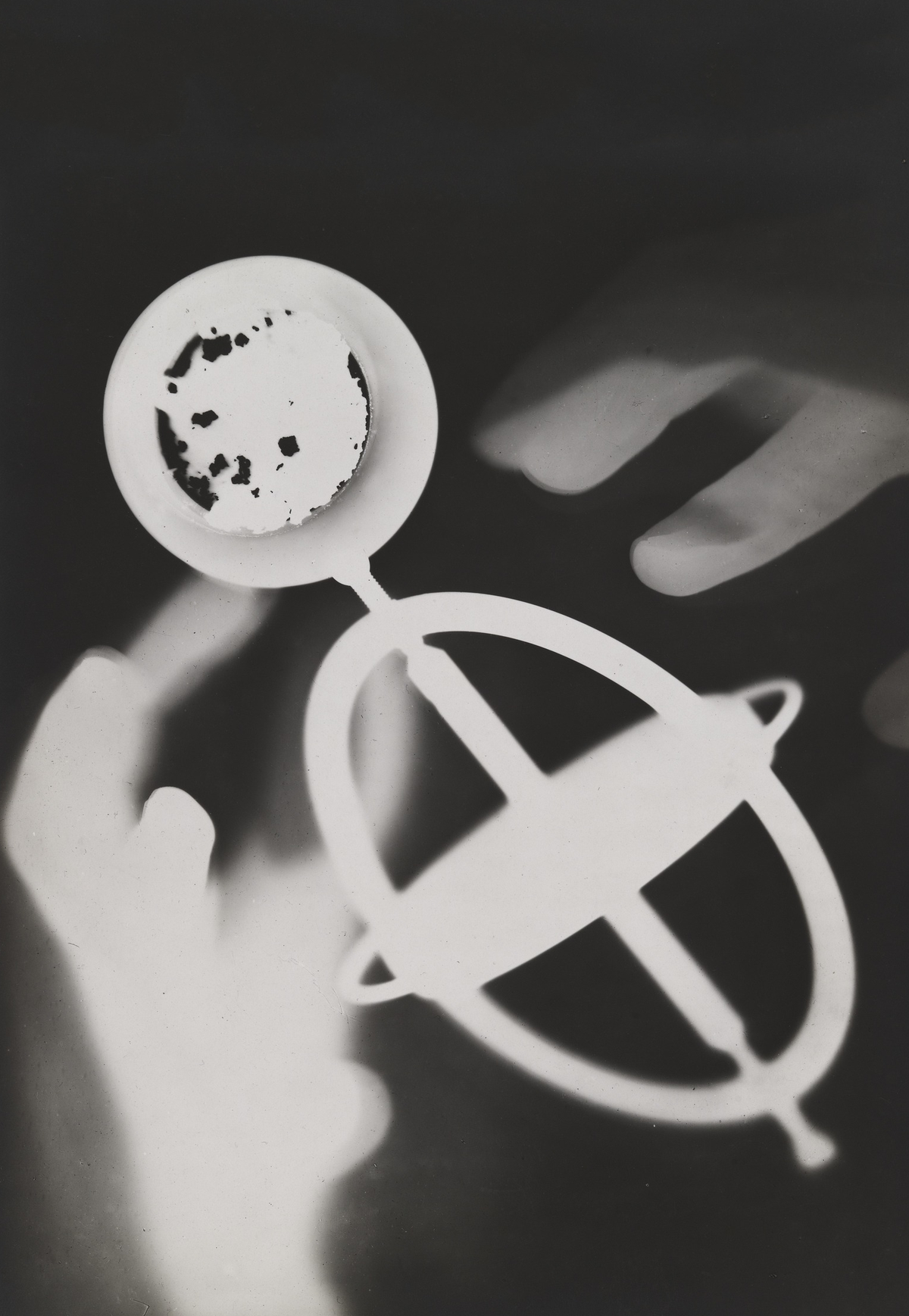 Intersecting circular rings and a small bright disc float among soft hand silhouettes on a dark background.