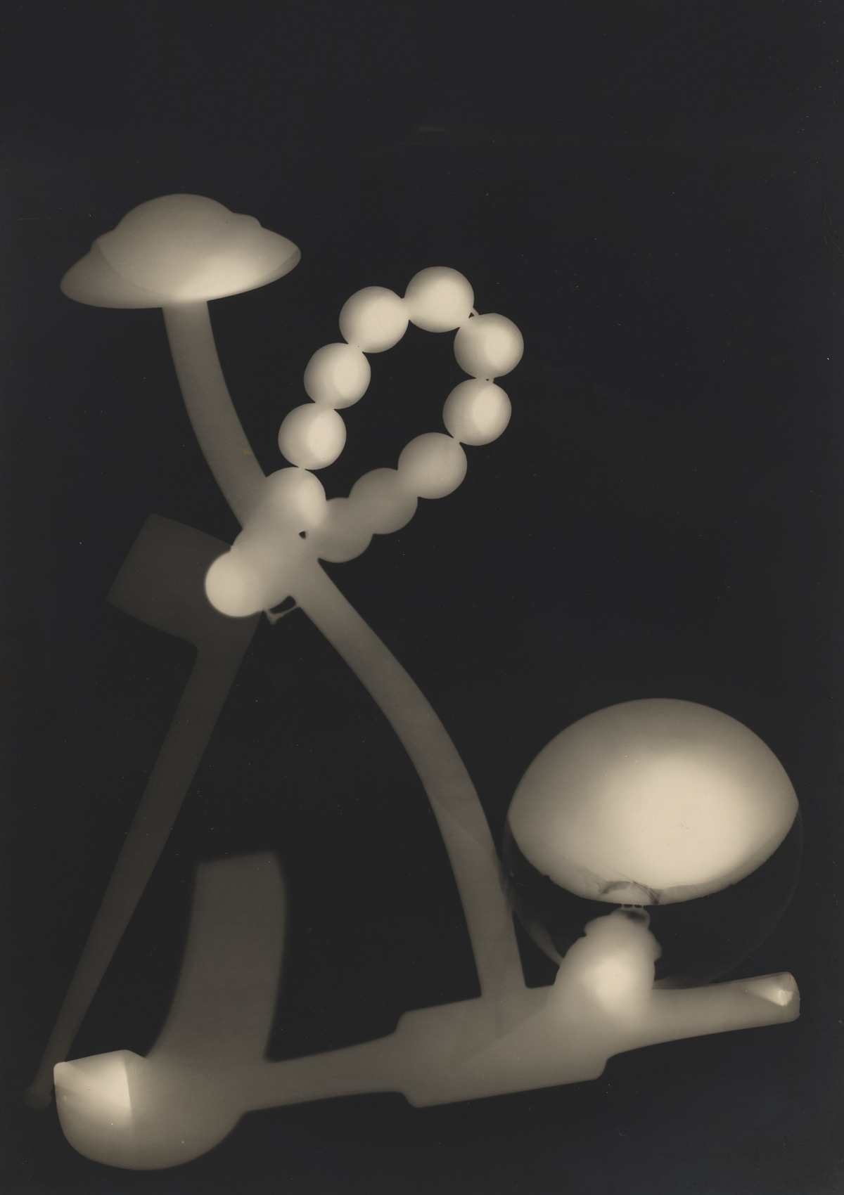 A loop of pale beads, rounded forms and branching silhouettes overlap in an experimental black-and-white photogram.