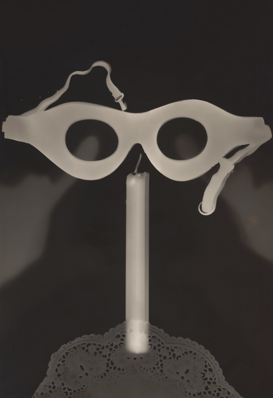 Pale spectacles hover above a candle and a lace-like circular base in a striking black-and-white photogram.